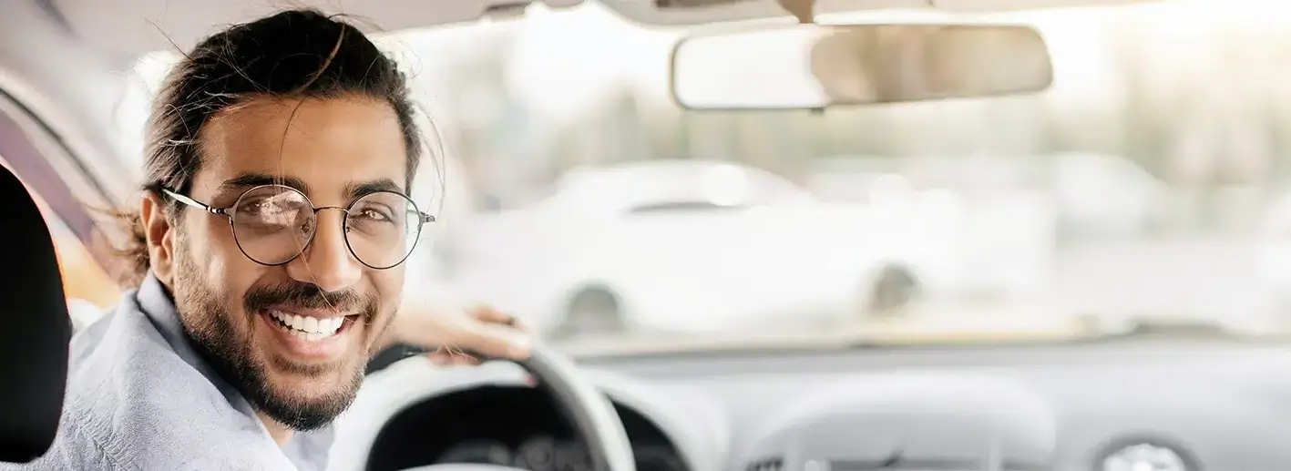 Ein gut gelaunter junger Taxifahrer schaut auf den Rücksitz und lächelt in die Kamera